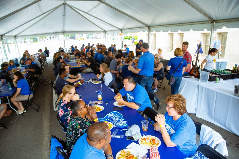 A wide shot of the gvsu party that is held right outside the stadium. Mostly everyone is seated and enjoying their food.